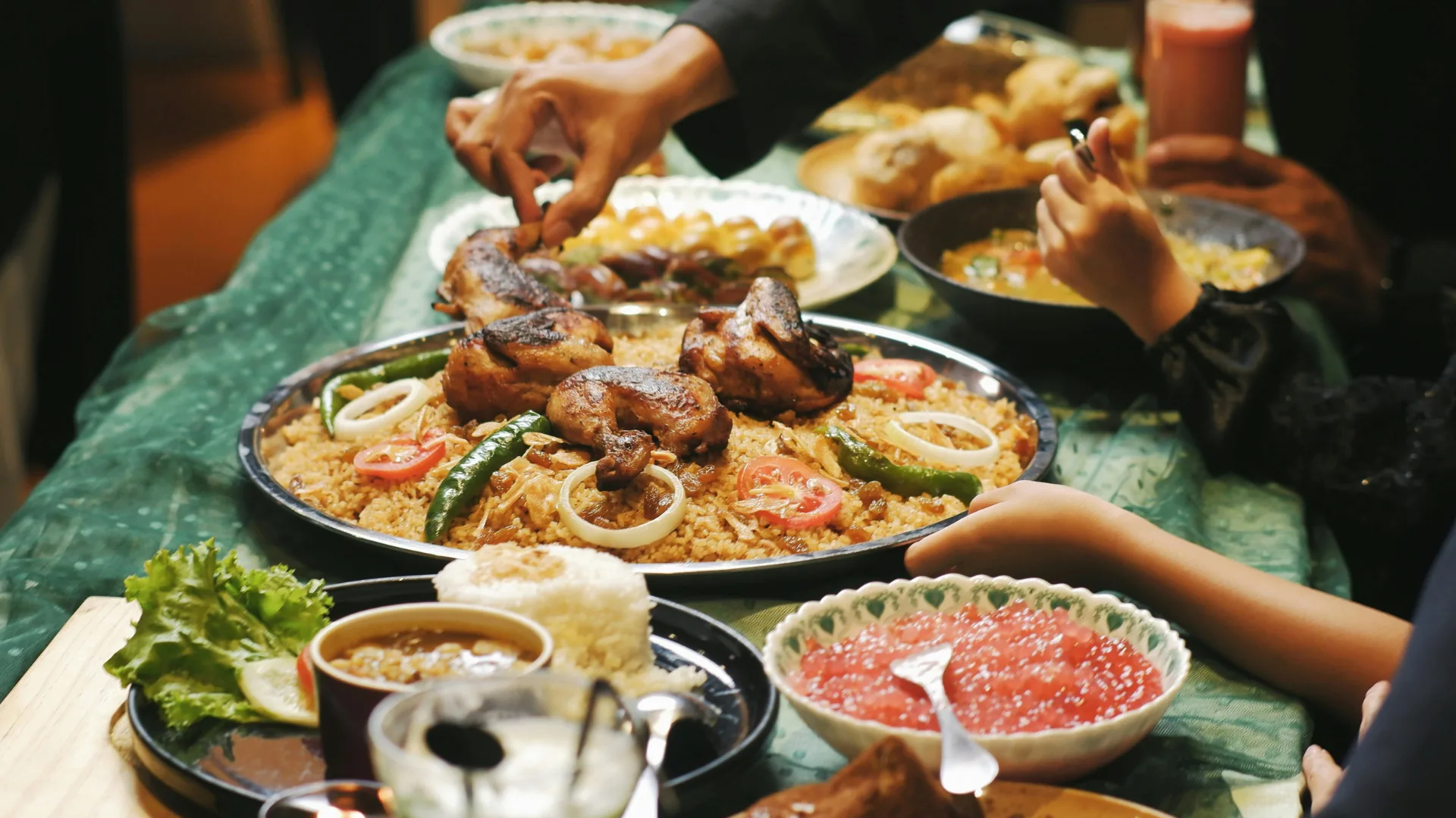 Handen die samen opscheppen van een rijk gedekte tafel met kip, rijst en mezze tijdens de iftar